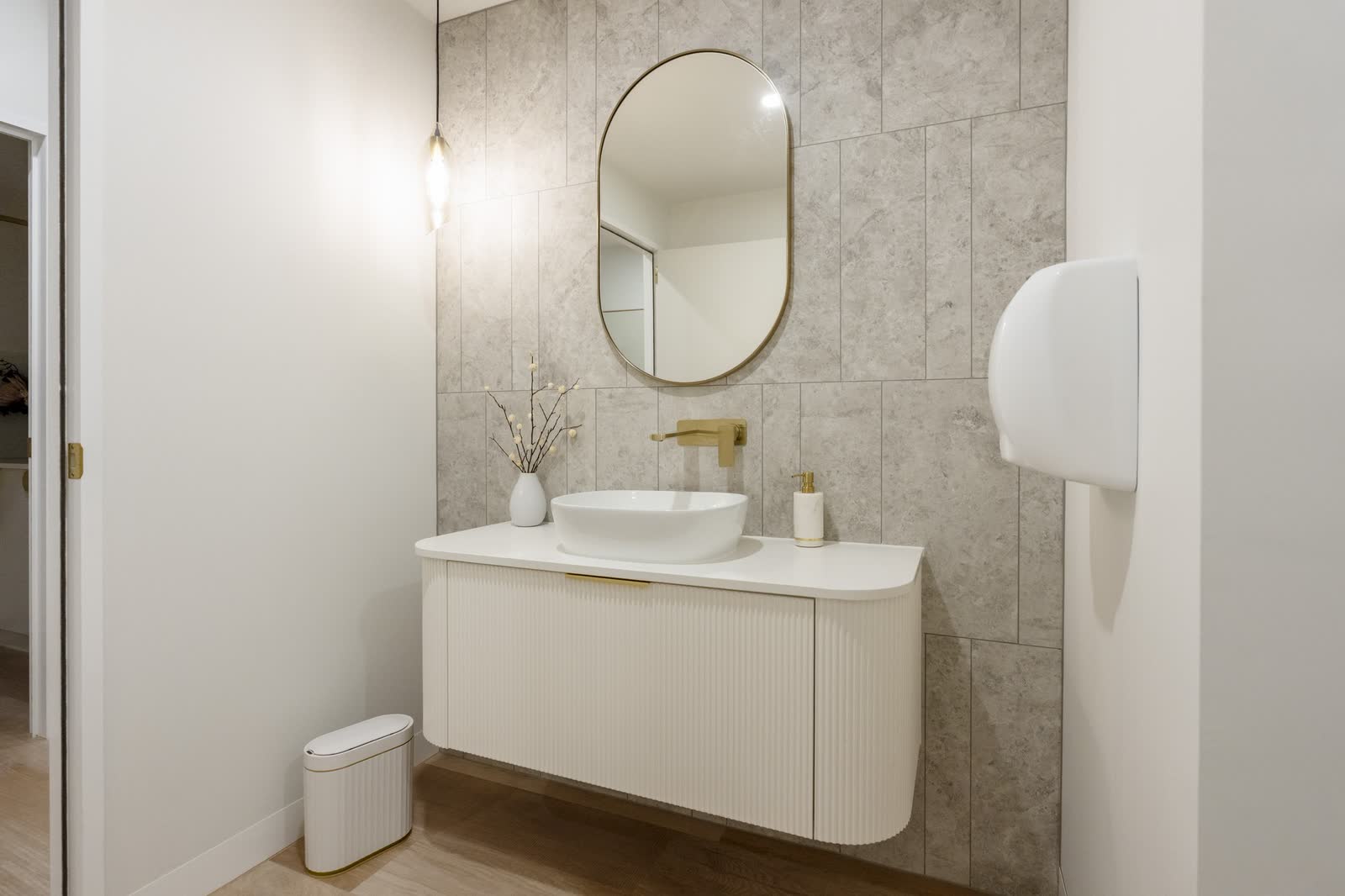 A hotel bathroom with a fluted timber vanity, vessel basin and oval mirror