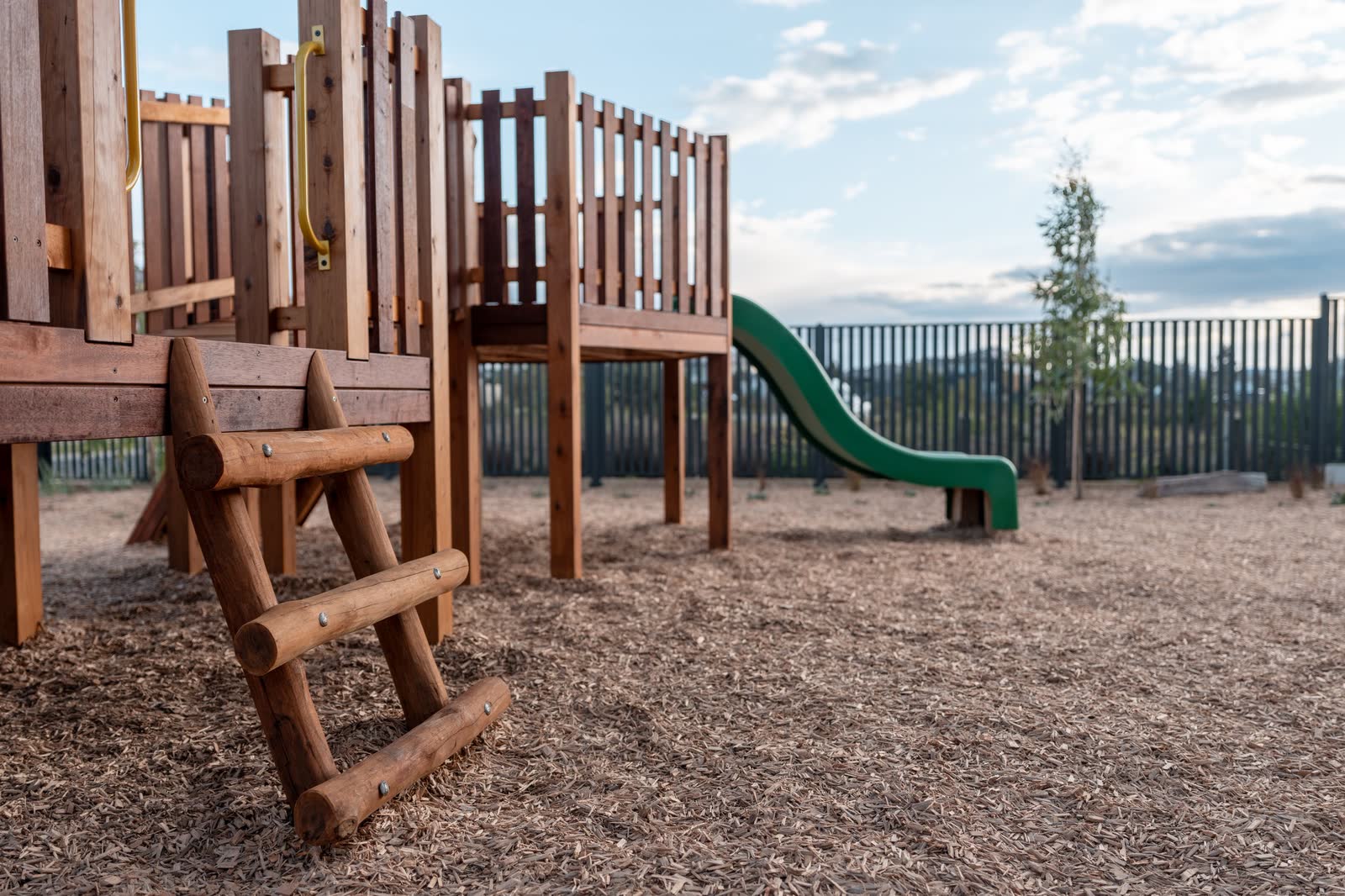 A timber playground tower with slide and climbing frame on soft fall