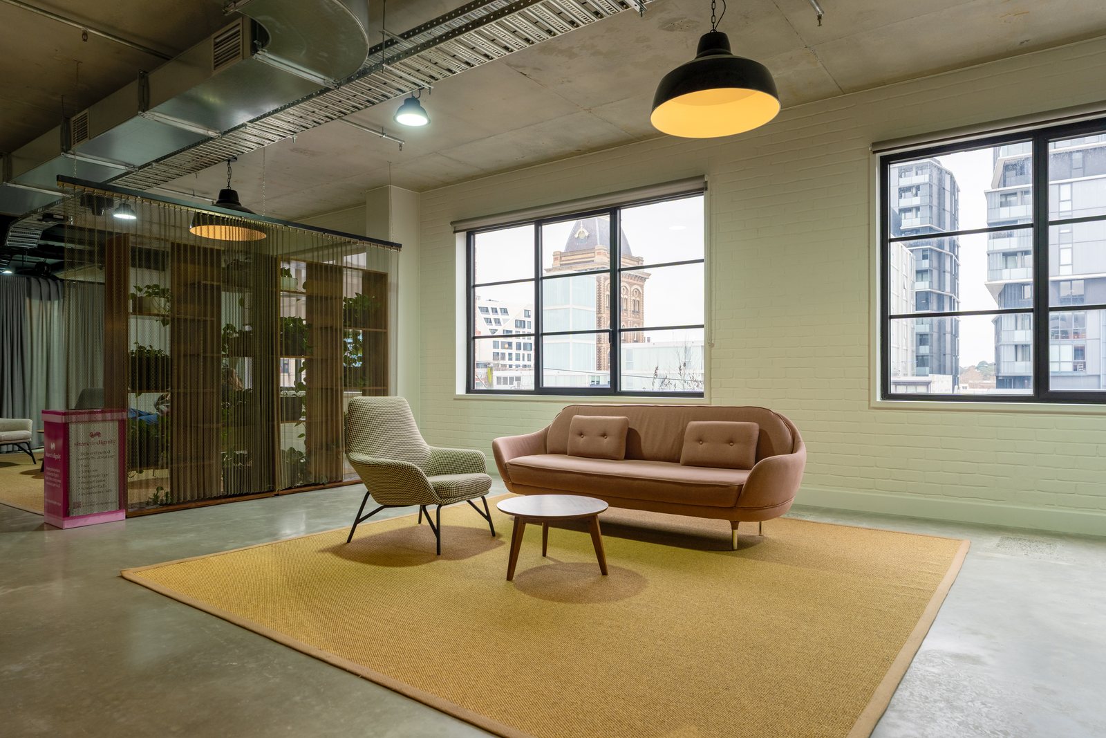 A blush sofa and armchair on a mustard rug beside a chain-mesh screen in an office fitout