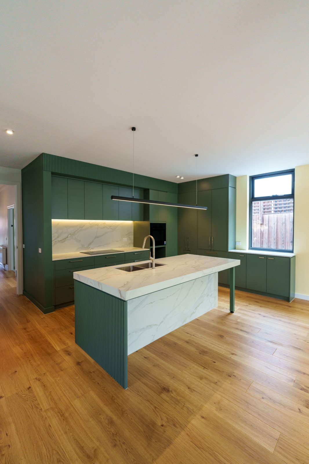 A green shaker kitchen with a stone island and integrated lighting