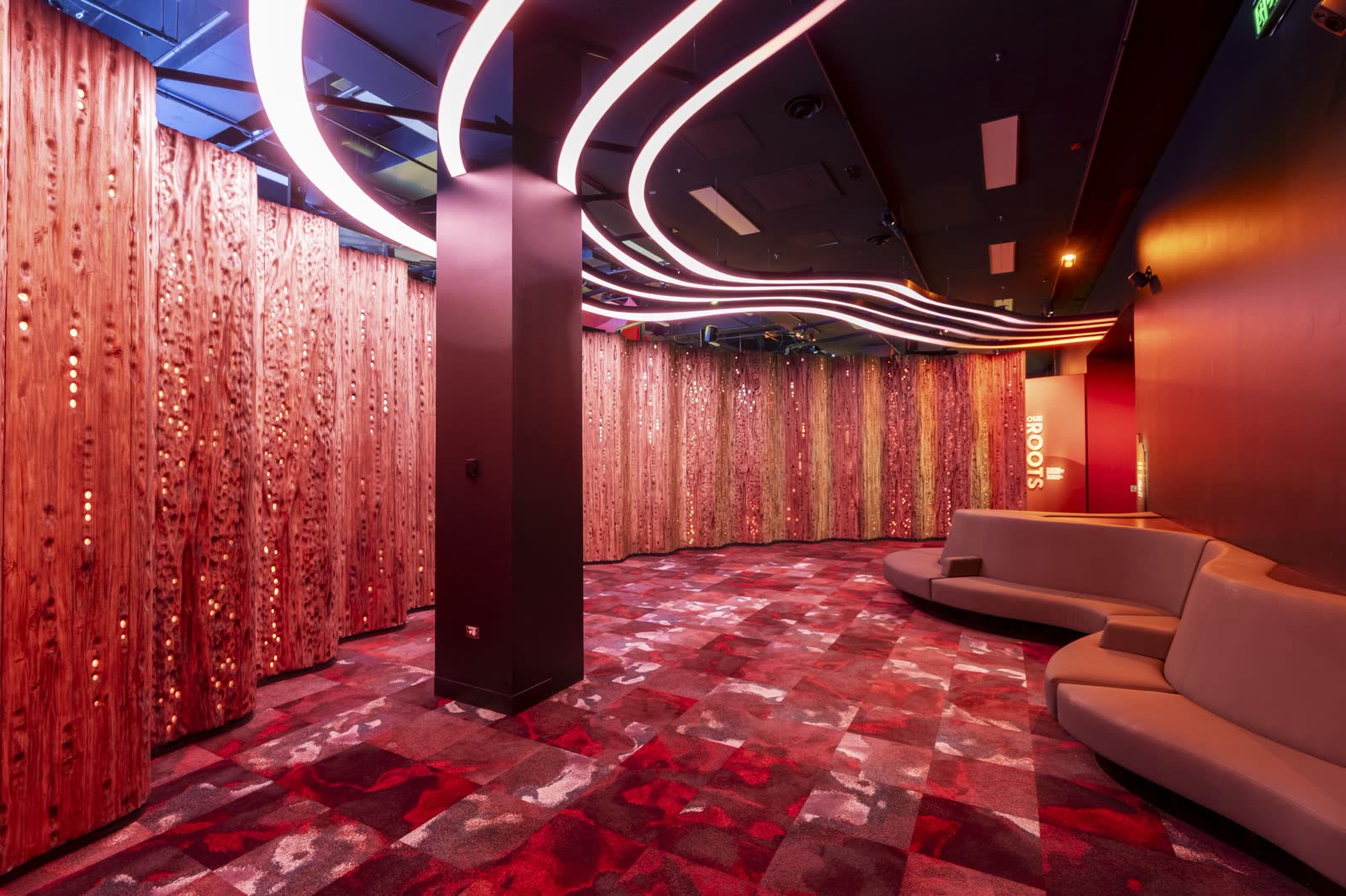 A red-lit museum gallery with a ribbon light installation and banquette seating
