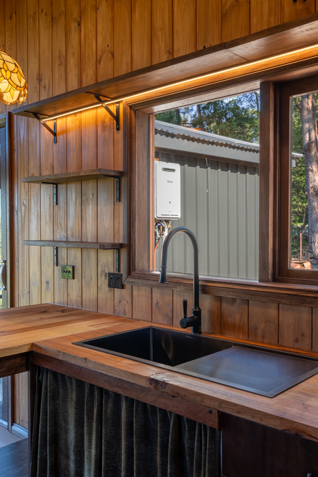 A black tap and undermount sink on a timber benchtop beneath a picture window
