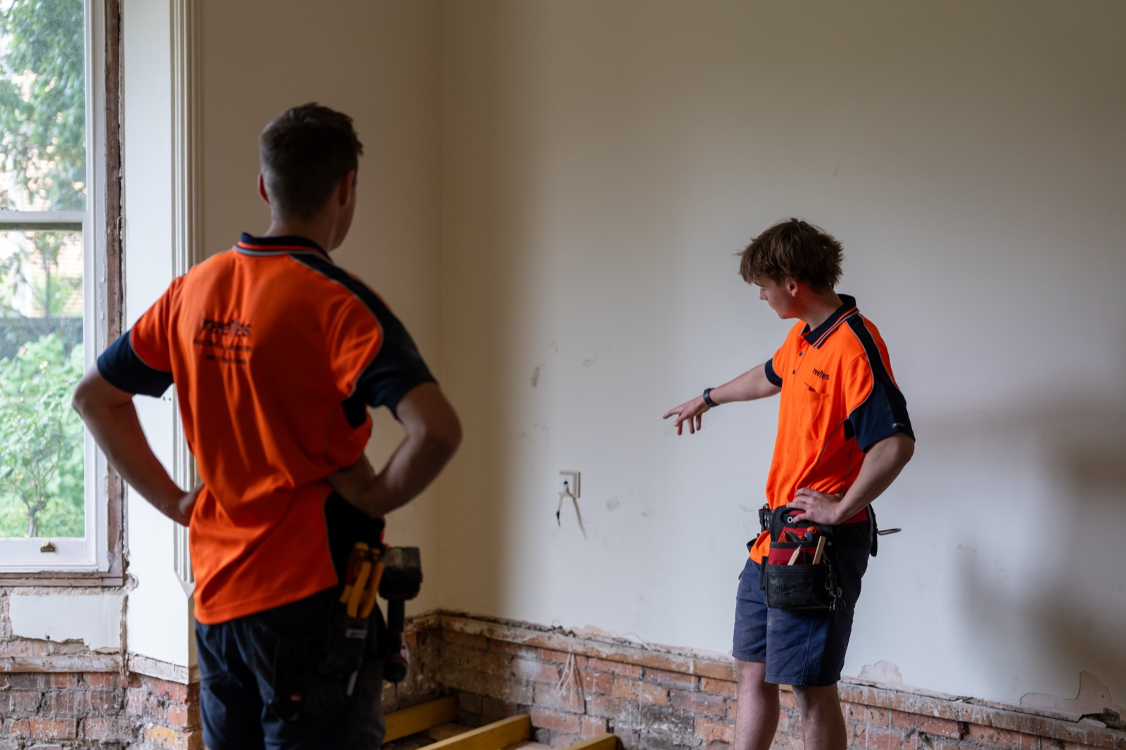 Two electricians talking through a rough in inside a stripped room