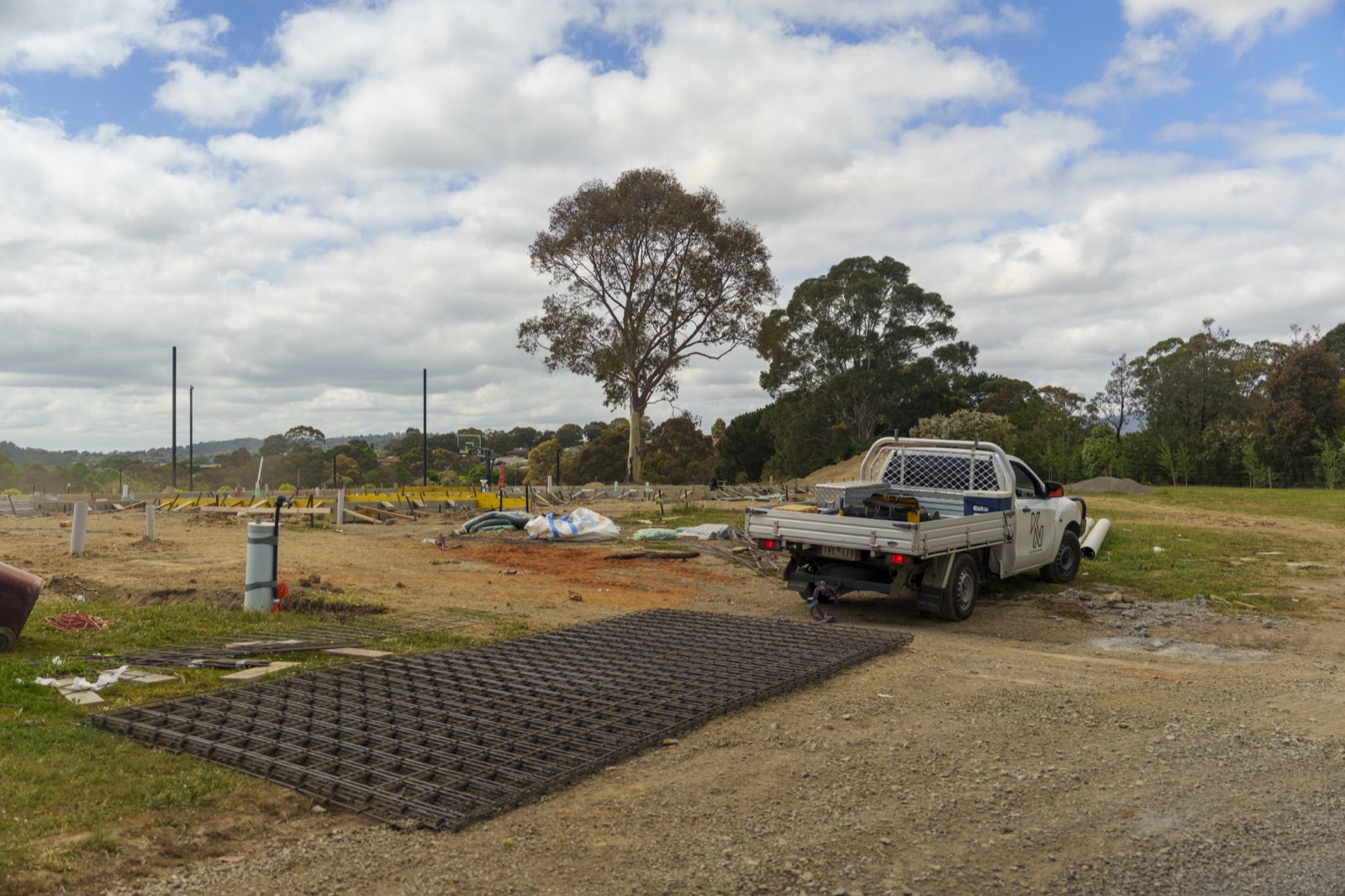 A ute and a geogrid access mat on a cleared site under a lone gum
