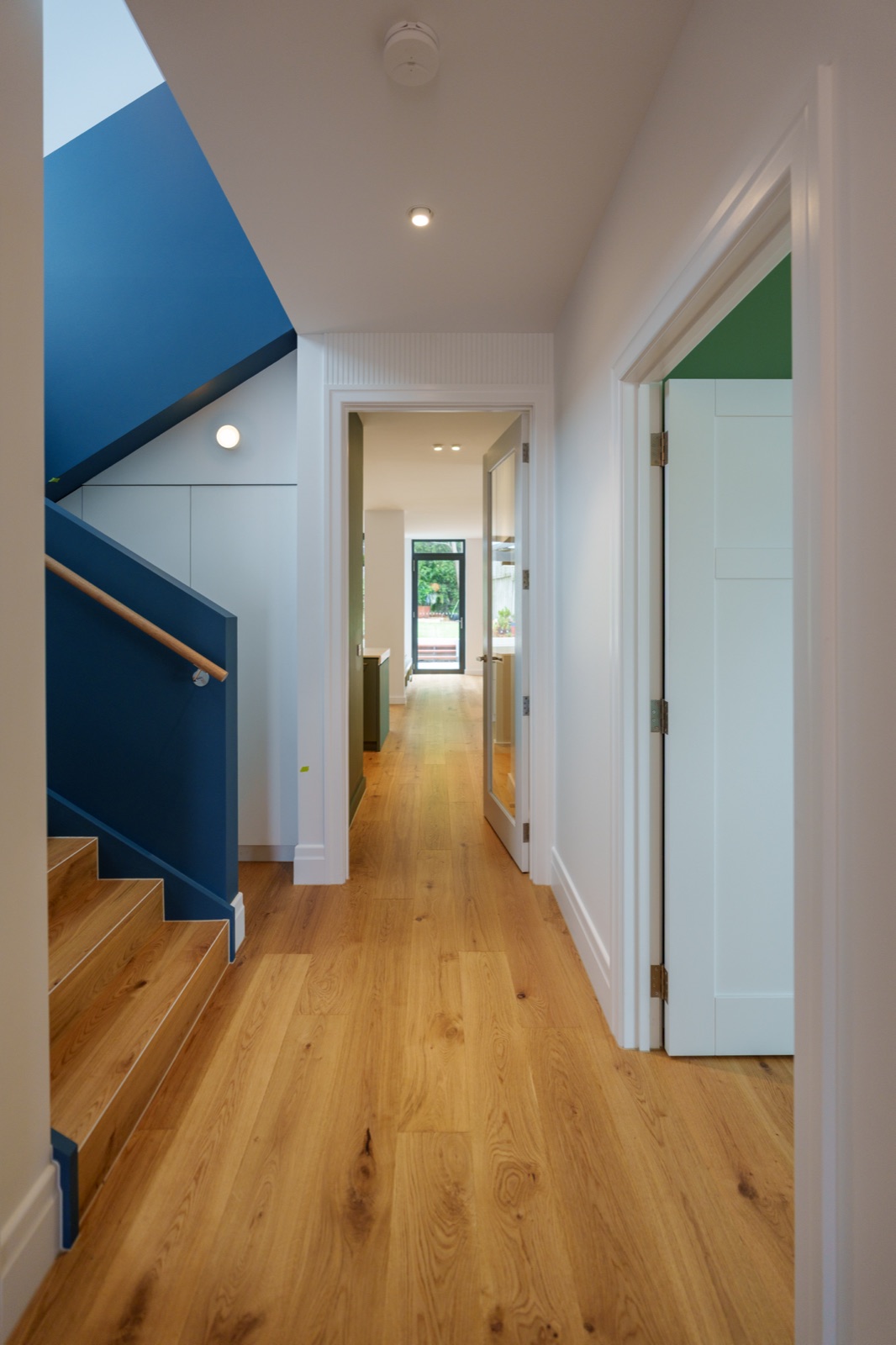A hallway in a finished home with oak floors and a navy stair void
