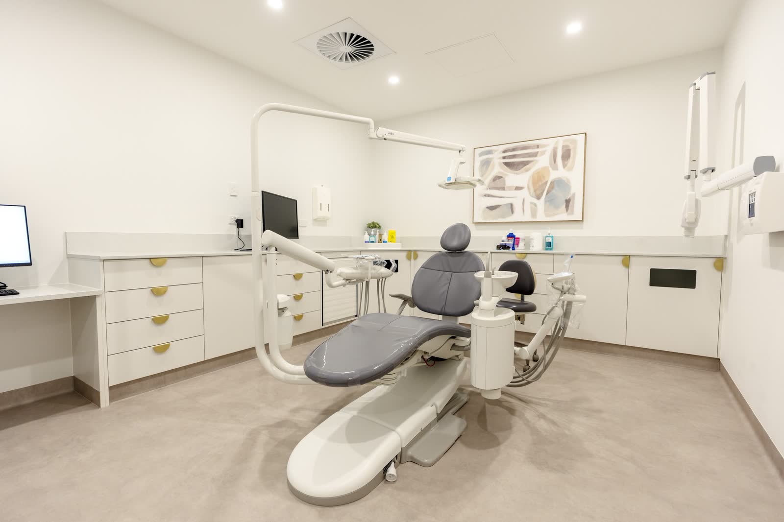 A dental surgery with treatment chair, overhead light and cabinetry