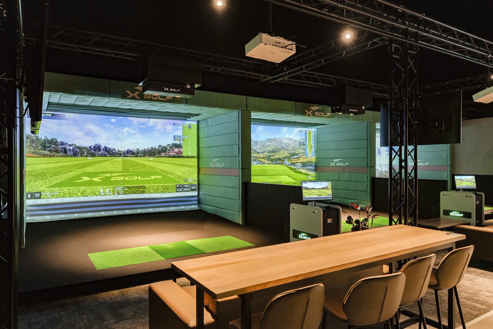 A long communal table facing the simulator screens at an XGOLF venue