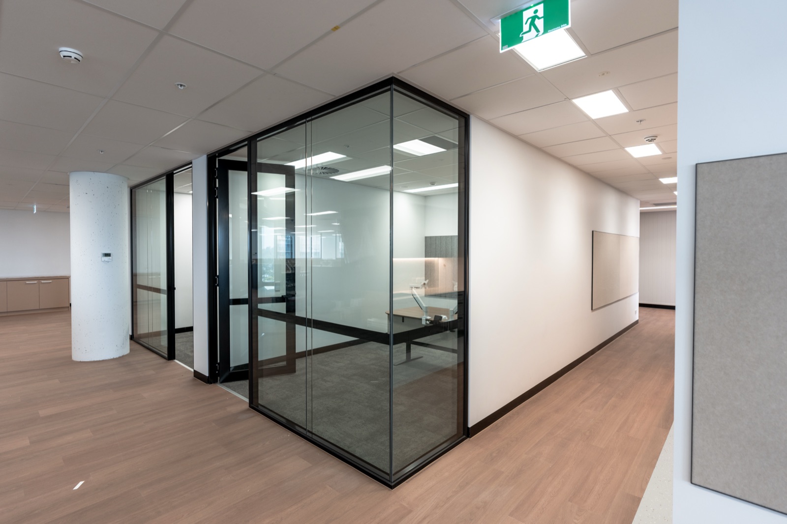 A glass partitioned meeting room off a carpeted office corridor