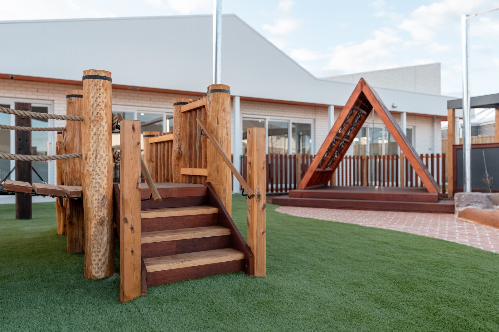 A timber climbing structure and A-frame play house on synthetic turf