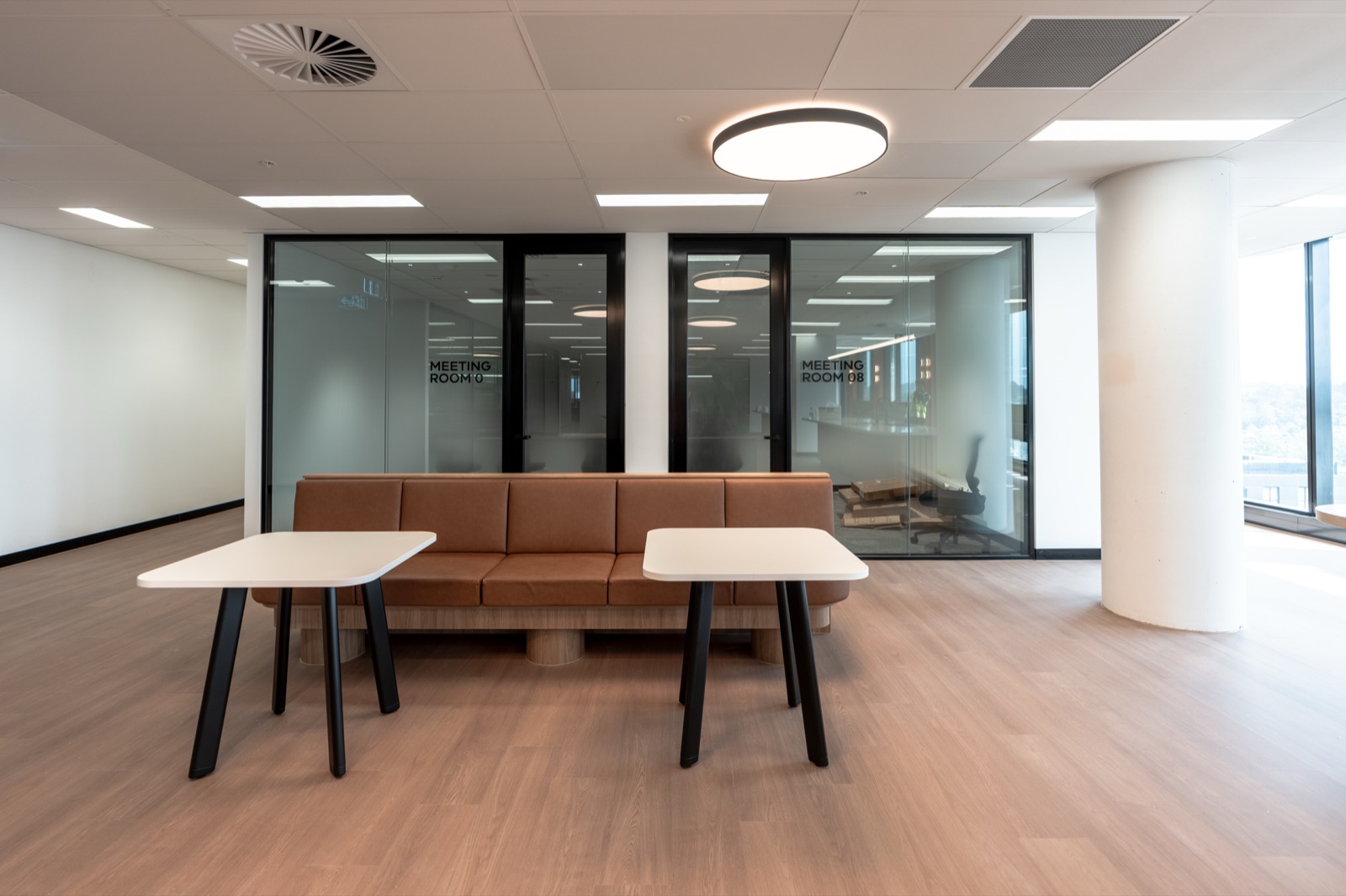 A tan leather banquette and cafe tables beside the glazed offices