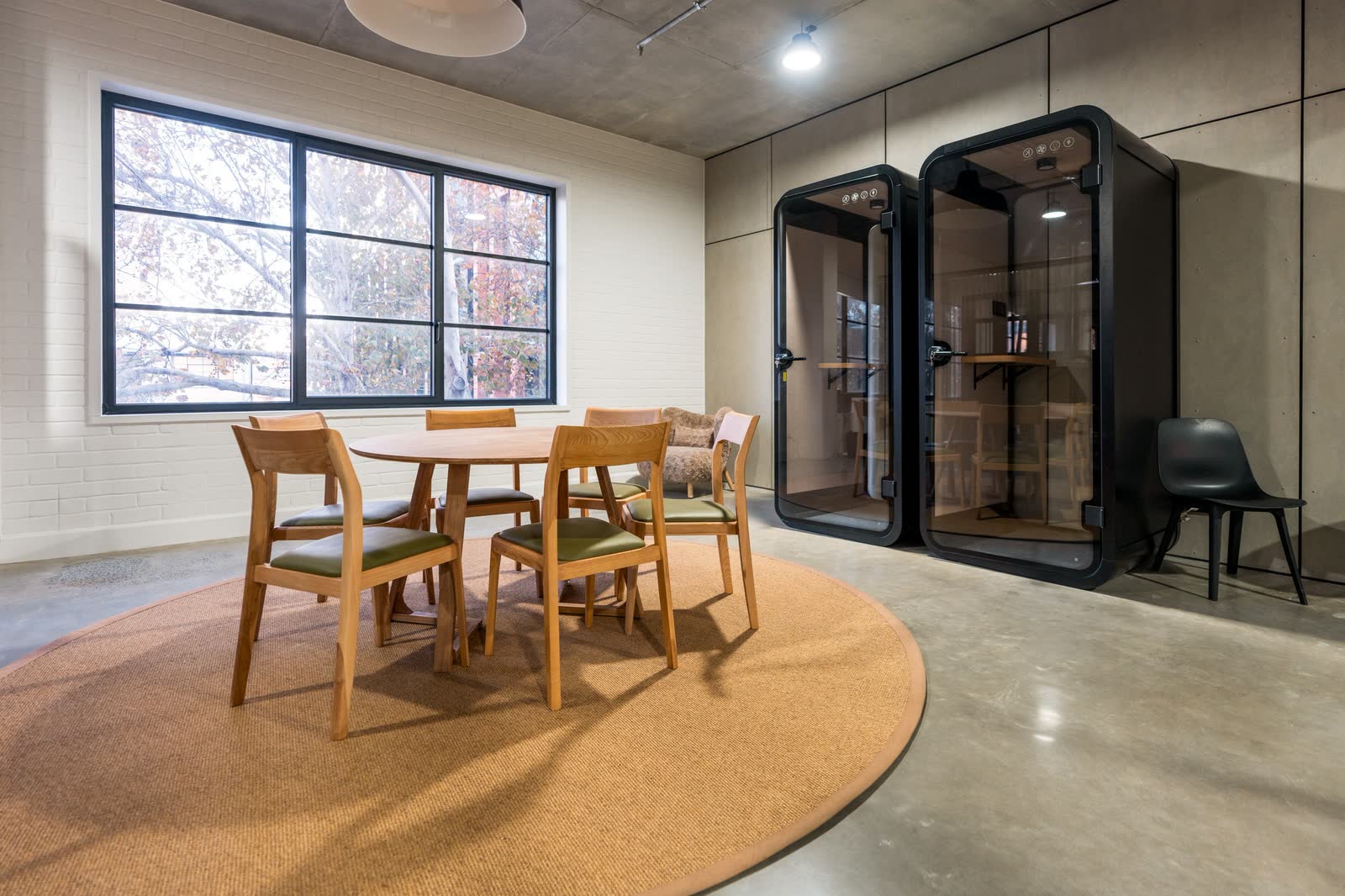 Acoustic phone booths and a meeting table on a round rug in an office fitout