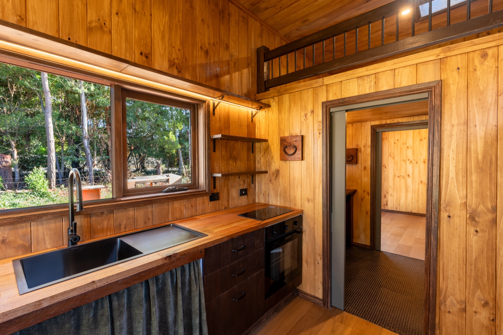 A tiny home kitchen in cypress lining with a black sink under the window