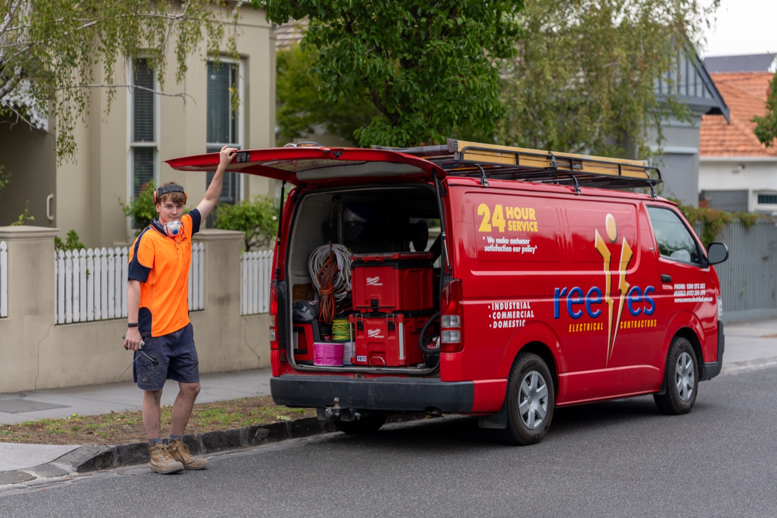 An electrician working from the back of an open service van on a suburban street