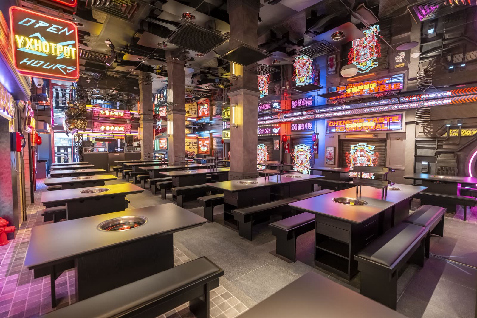 Rows of hotpot tables beneath dense neon signage in a themed restaurant