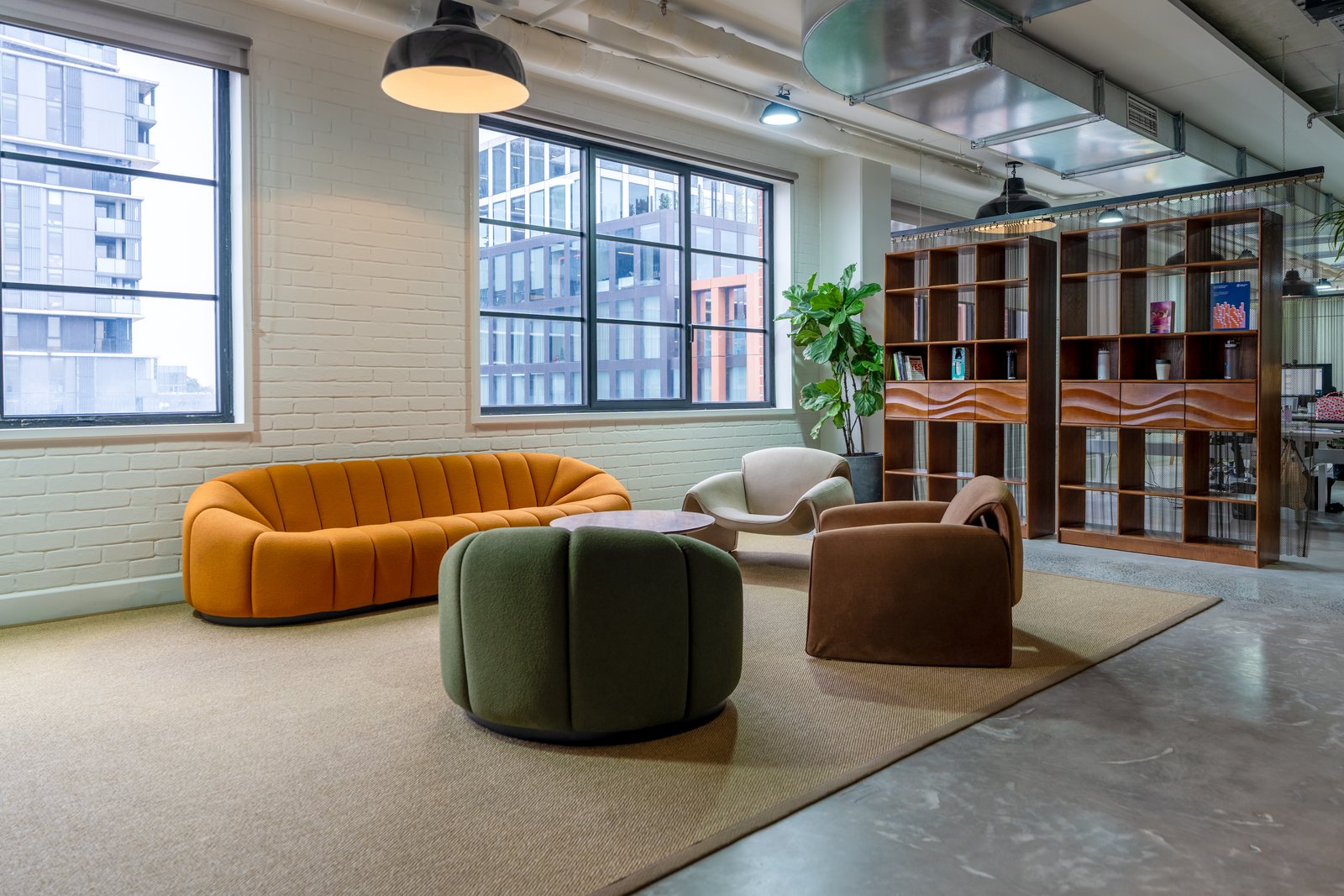 A breakout lounge with a curved orange sofa, green ottoman and timber shelving in an office fitout