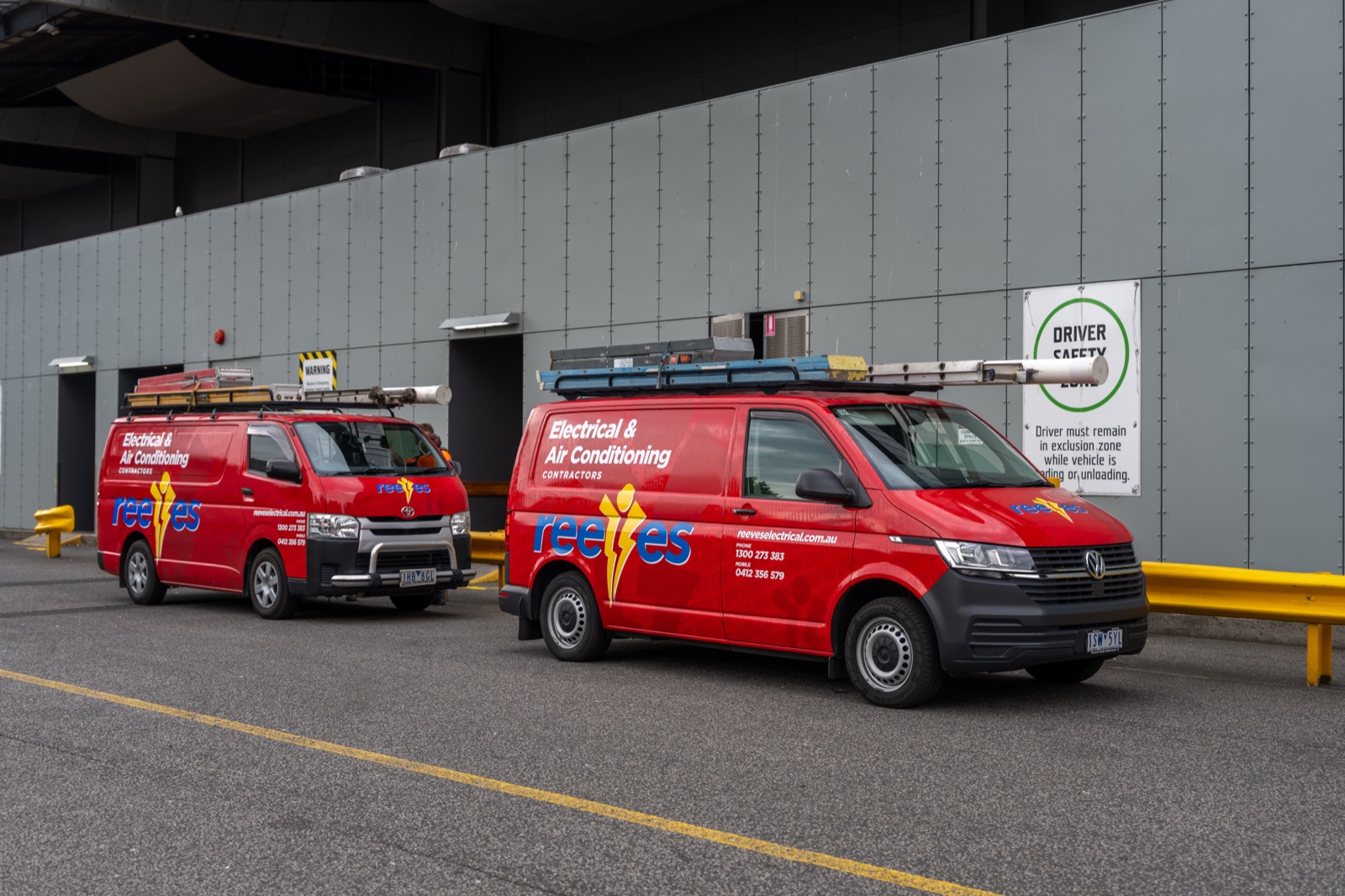 Two branded electrical service vans parked at a warehouse loading dock