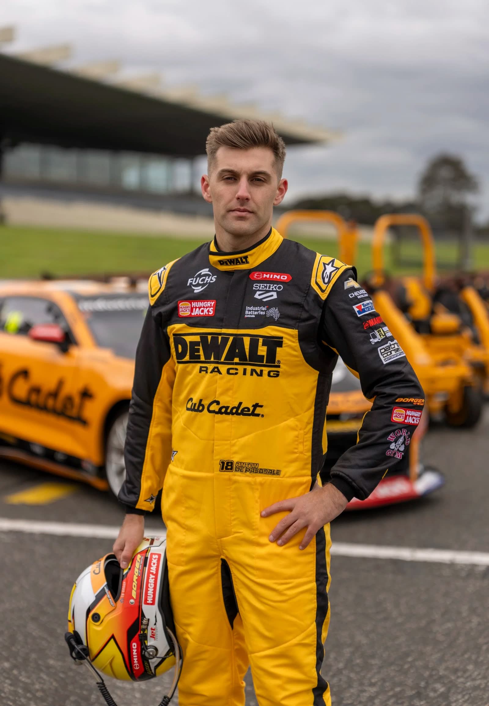 A racing driver in DeWALT Racing suit holding a helmet beside the cars at a circuit