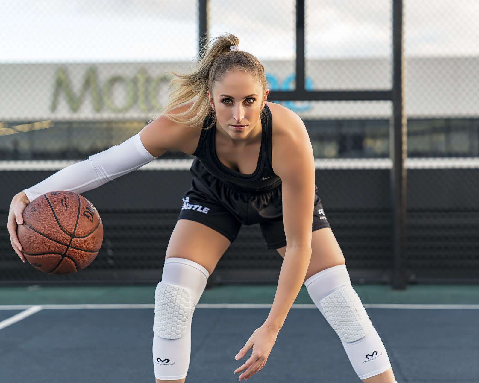 A basketball player in a defensive stance with the ball on an outdoor court
