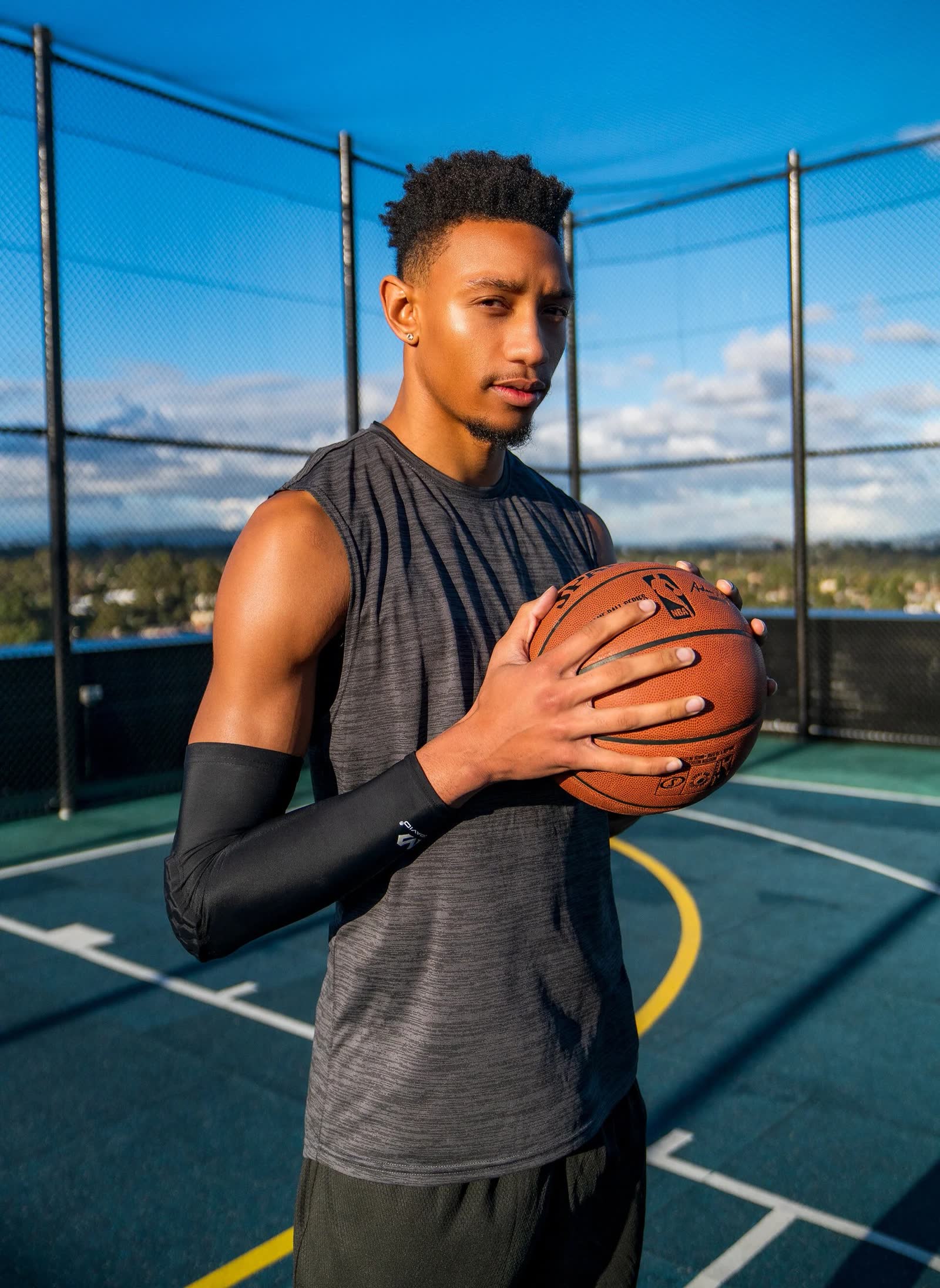 A basketball player holding the ball on a rooftop court against a blue sky