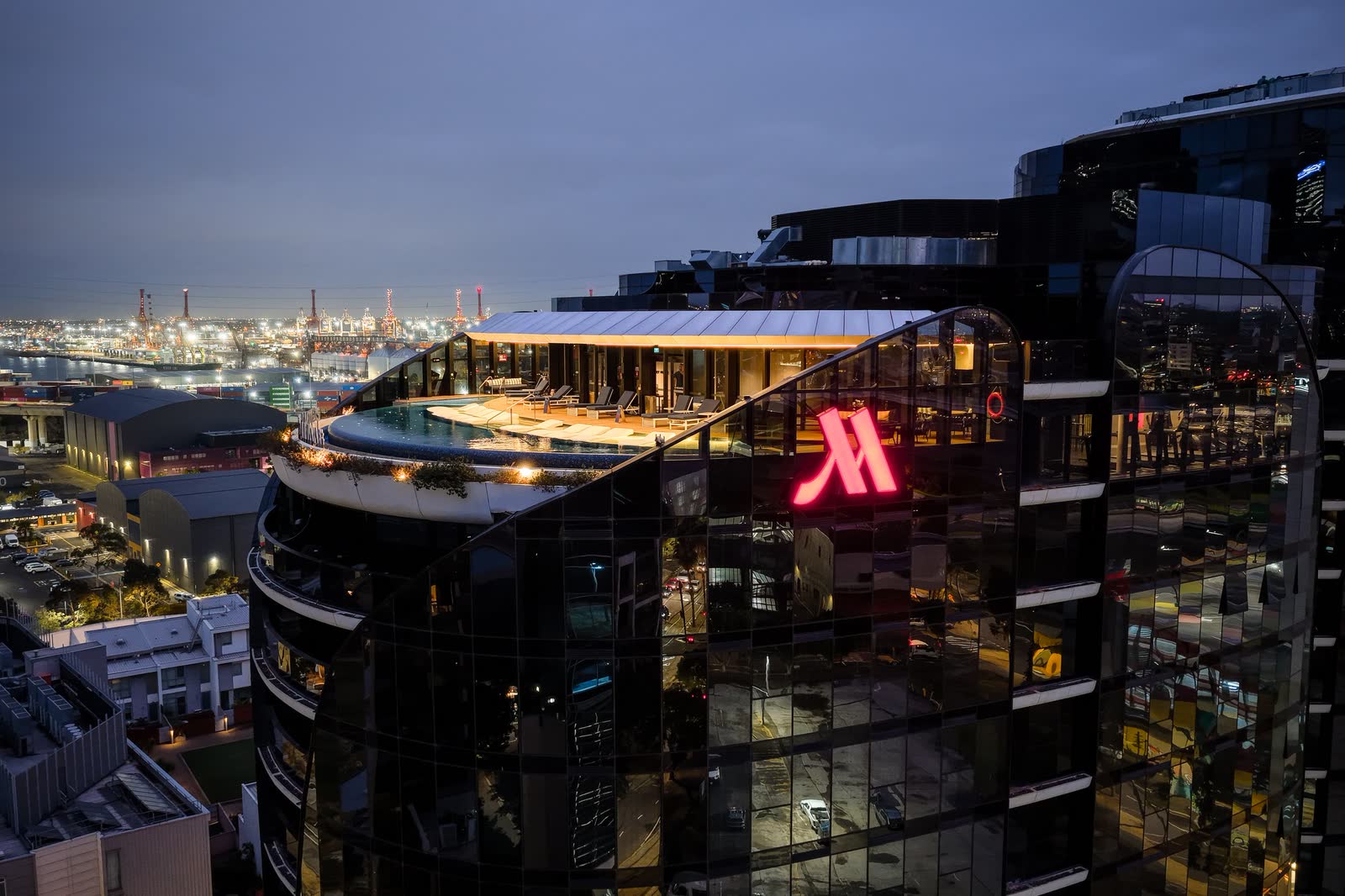 Aerial view of a waterfront hotel and its lit rooftop bar at dusk, Melbourne