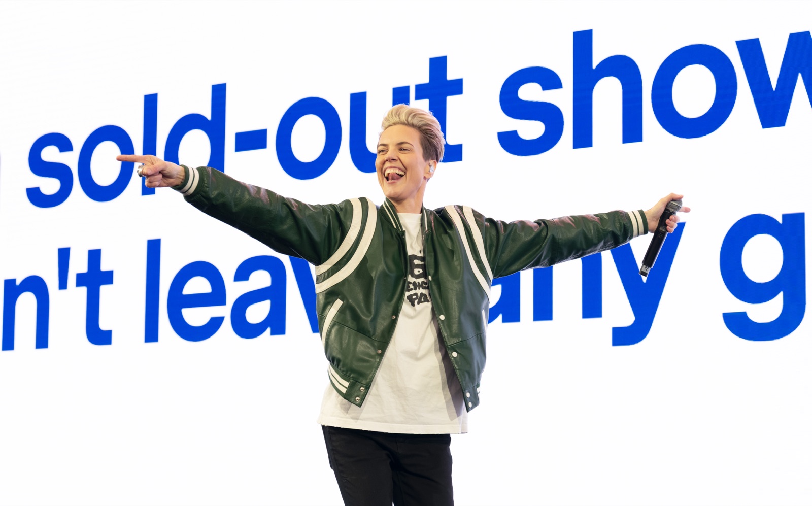 A keynote speaker mid gesture against a full width screen