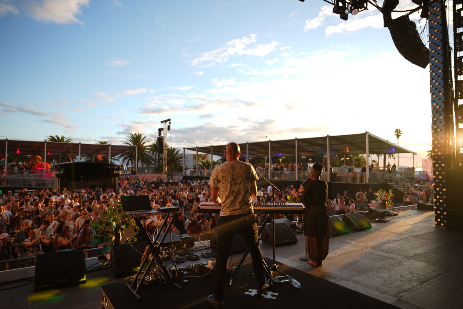 A festival crowd at an outdoor stage at sunset