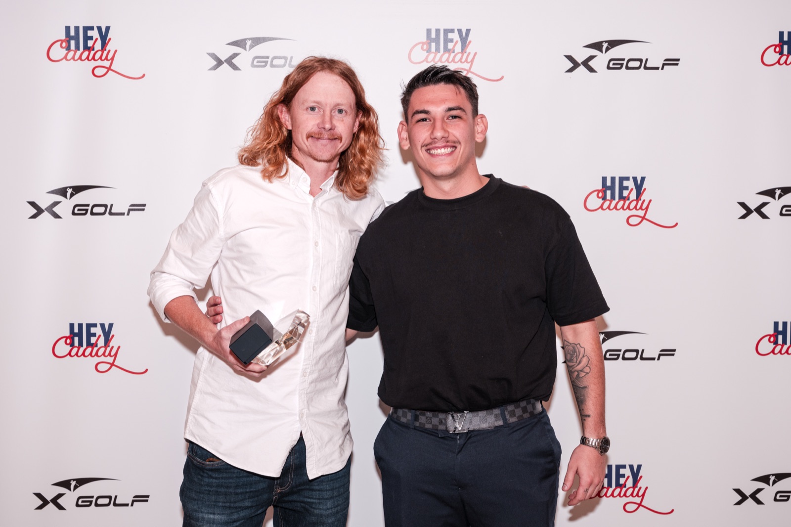Two guests with an award at a branded media wall