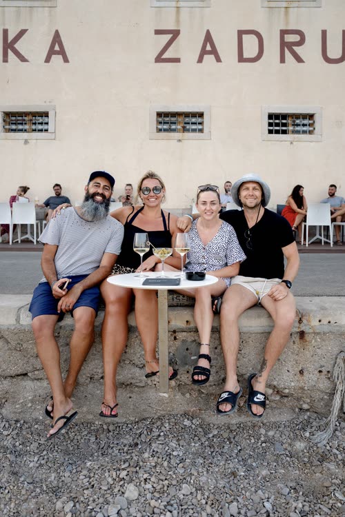 Friends sitting with wine outside a stone building on a Croatian waterfront