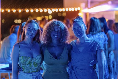 Three women at a party under festoon lights in blue light, Croatia