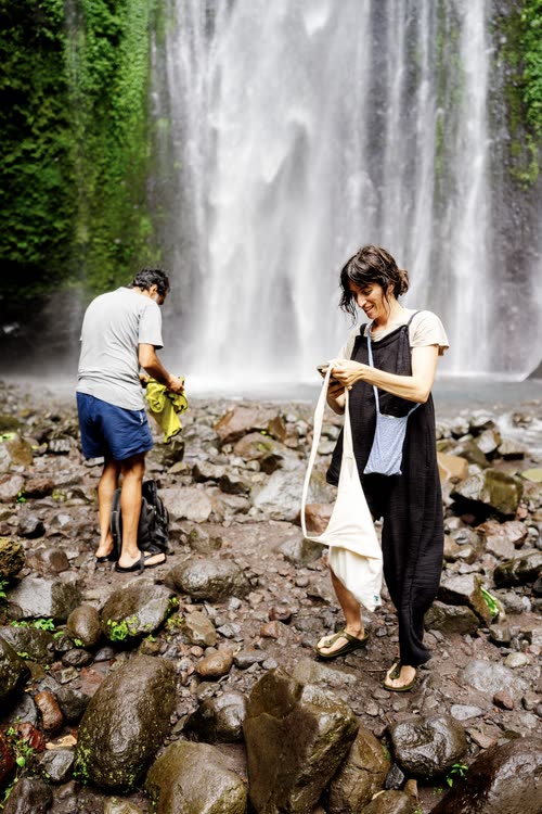 Two travellers picking their way across the boulders below a waterfall