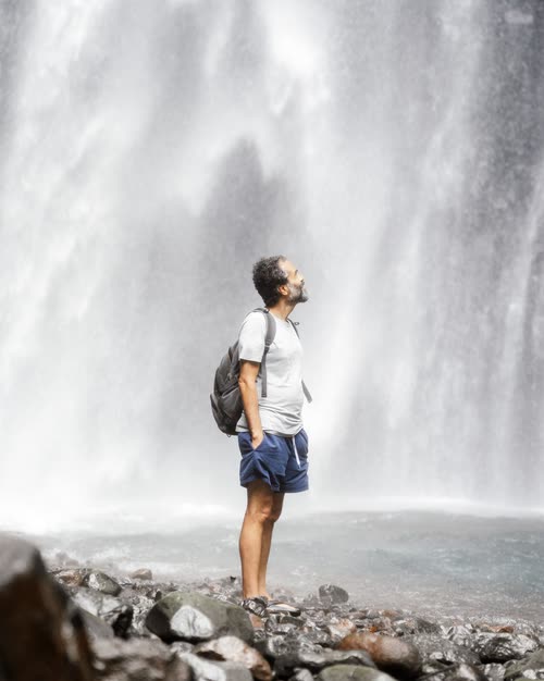 A man standing in the spray at the base of a large waterfall, Lombok