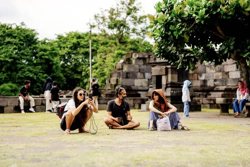 Visitors sitting on the lawn beside the stone ruins of a Javanese temple