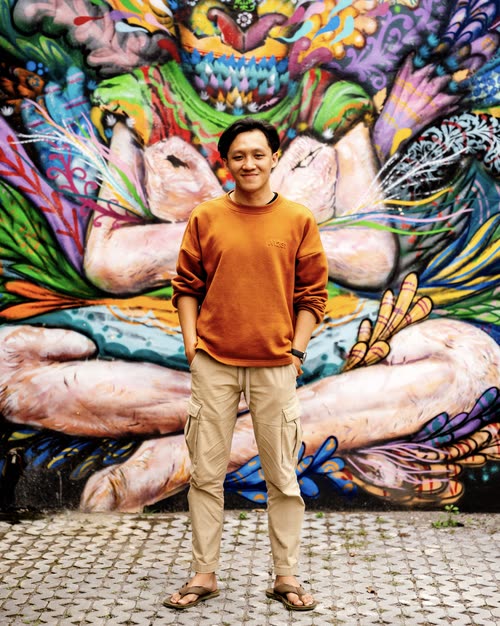 A man standing in front of a large painted mural of a seated figure