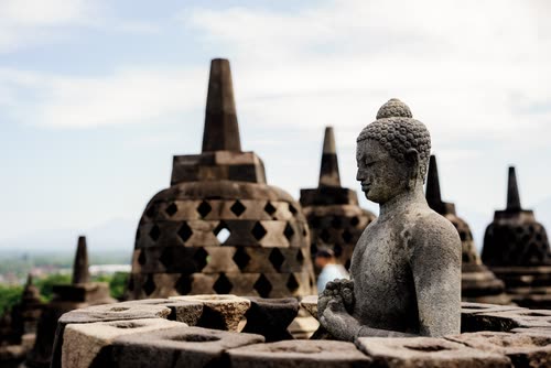 A seated stone Buddha beside the latticed stupas of Borobudur, Java
