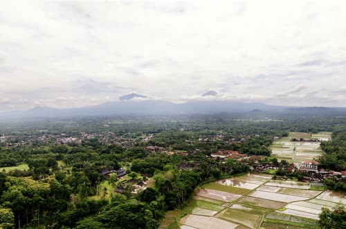 Aerial view over Javanese farmland and villages toward distant volcanoes