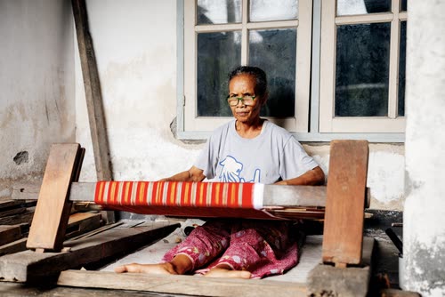 A weaver working a backstrap loom outside a village house in Lombok