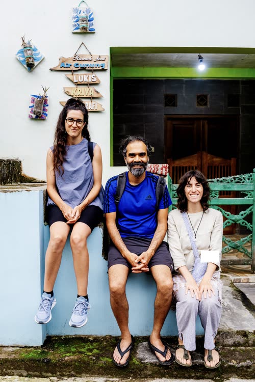 Three travellers seated on a low wall outside a village homestay in Indonesia