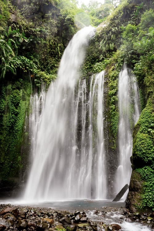 A wide waterfall spilling over a mossy cliff into a shallow pool, Lombok