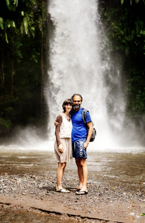 A couple standing on the stones in front of a wide waterfall, Lombok