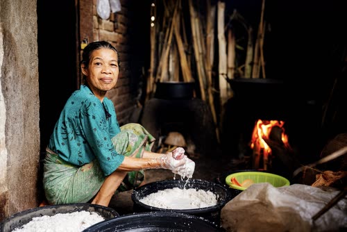 A woman working over rice at a wood-fired village kitchen in Indonesia