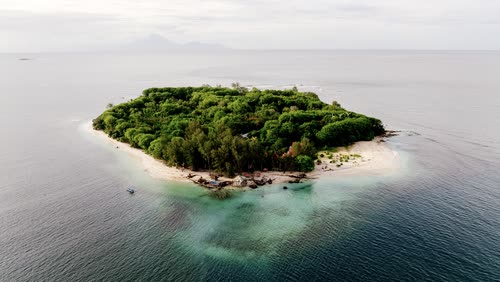 Aerial view of a small forested island ringed by reef and pale sand, Indonesia