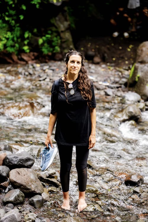 A woman standing barefoot in a shallow rocky river in Lombok