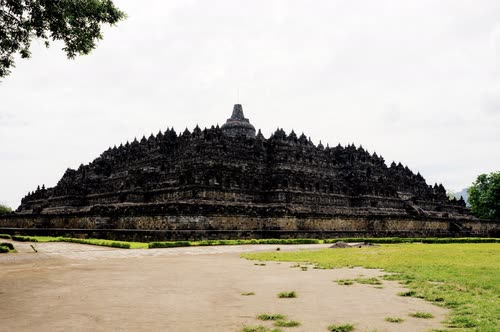 The stepped stone mass of Borobudur seen across open ground, Java