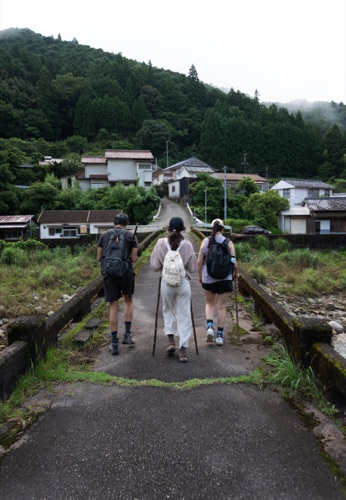 Three hikers walking into a mountain village along a narrow road