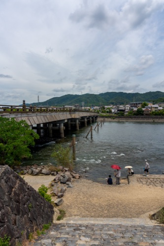 The long wooden bridge over the Uji river with hills behind and people on the bank
