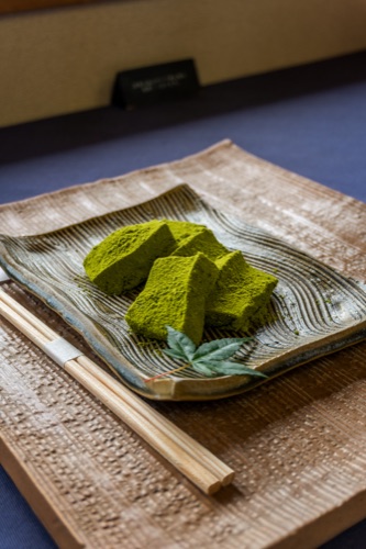 Cubes of matcha warabi mochi on a ridged ceramic plate with chopsticks