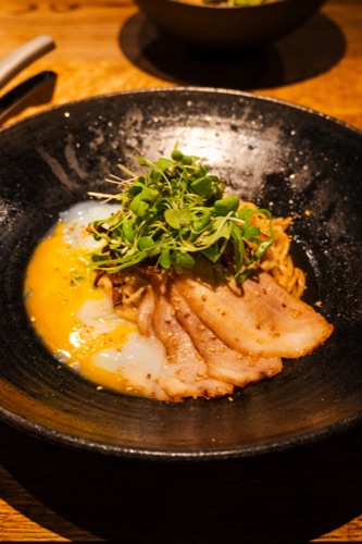 A bowl of soft egg, sliced pork and micro herbs on noodles, photographed from above