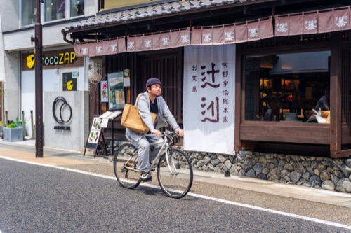 A cyclist passing the dark timber frontage of a tea merchant in Uji
