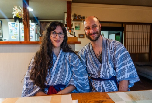 A couple in blue yukata smiling at a timber counter in a country inn