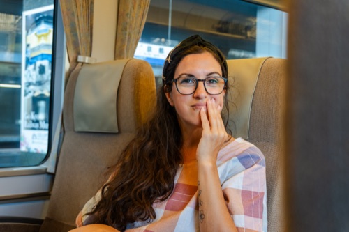 A woman in glasses and a checked shirt at a train window, hand to her face